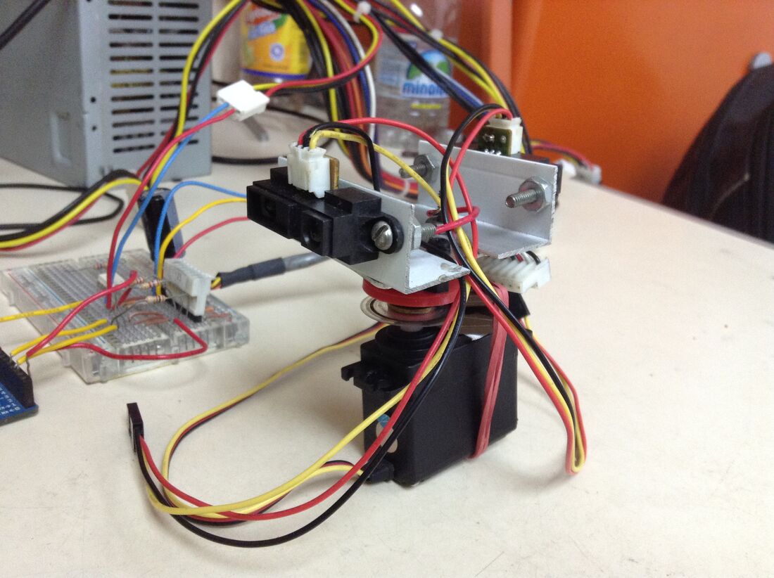 Close-up of the sensor bracket: two black Sharp infrared distance sensors bolted to an aluminium bar on top of the servo