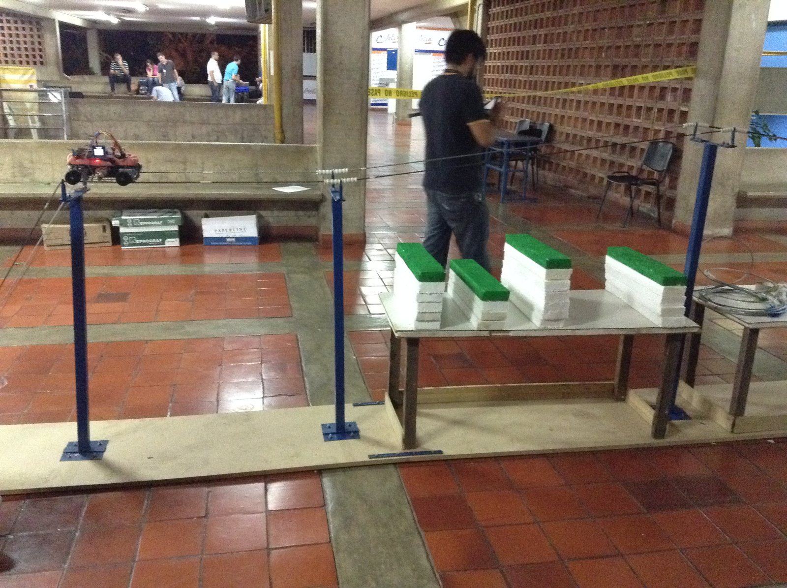 The robot E-wanna riding the twin steel cables of a mock high-tension power line at night, headlights on, during the UNETBots 2015 competition