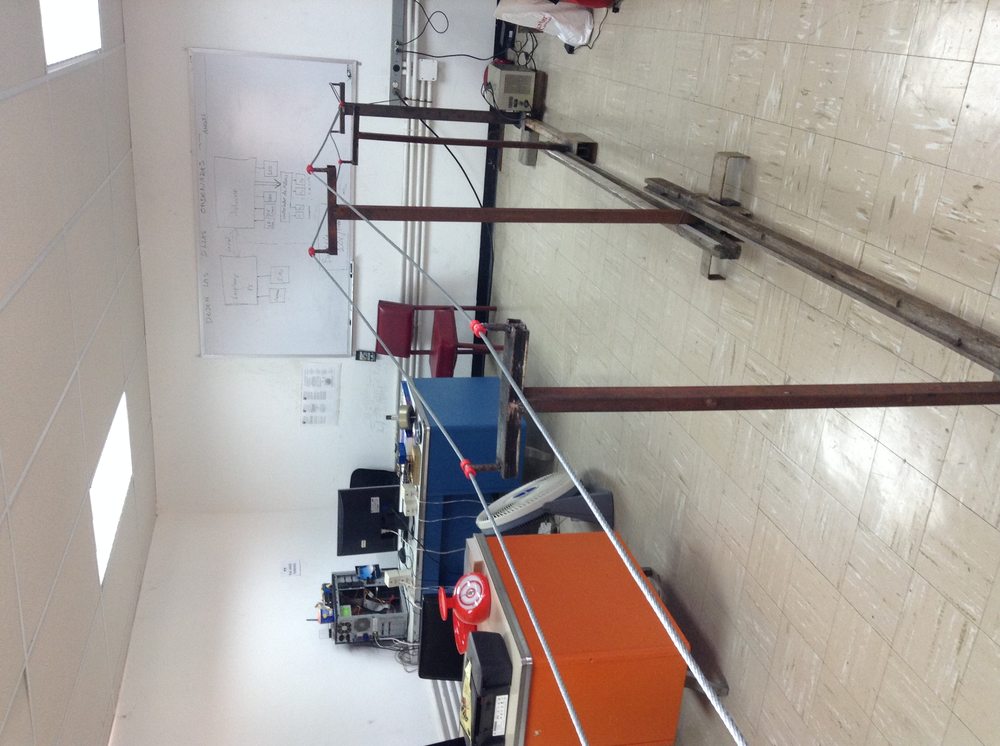 The team's own classroom test rig: a single cable strung between two welded towers, with a hand-drawn system architecture diagram on the whiteboard behind it