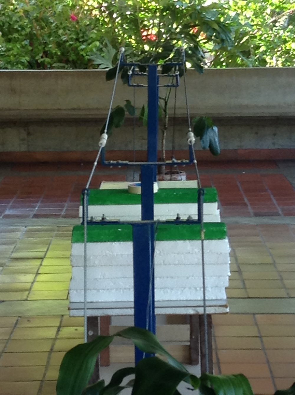A small home-built mock power-line tower with a wooden mast, twin steel cables, and foam blocks standing in for roadside vegetation, used to test the robot before the real rig was available