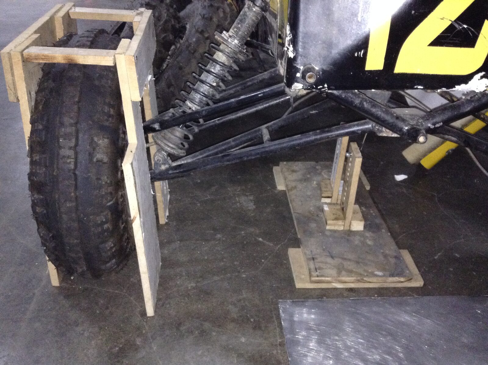 A Baja SAE USB buggy on a wooden alignment jig, one knobby tyre held in a wooden cradle and a stand under the front A-arm
